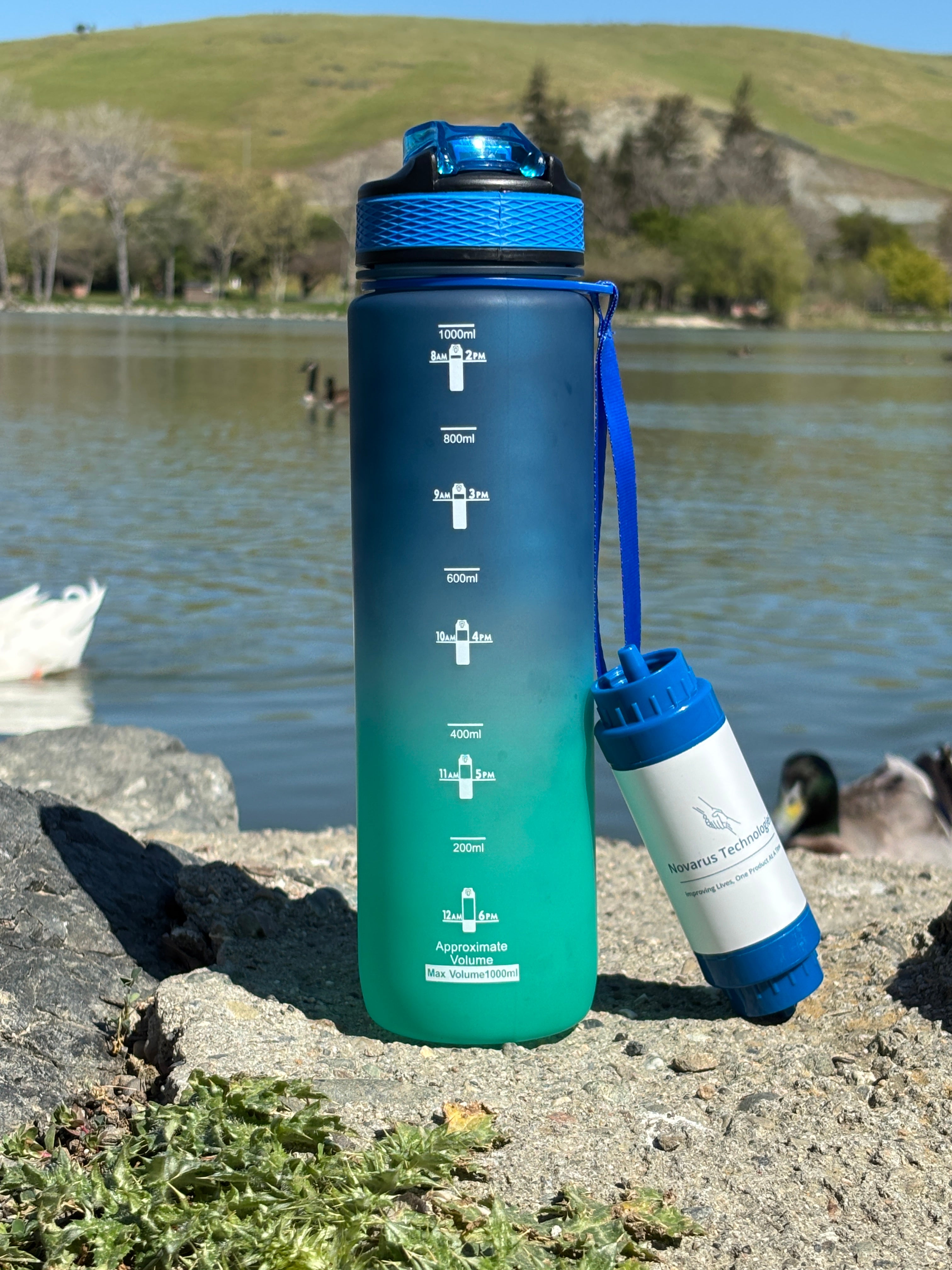 Gradient blue to green water bottle with blue cap on a concrete surface near a body of water.