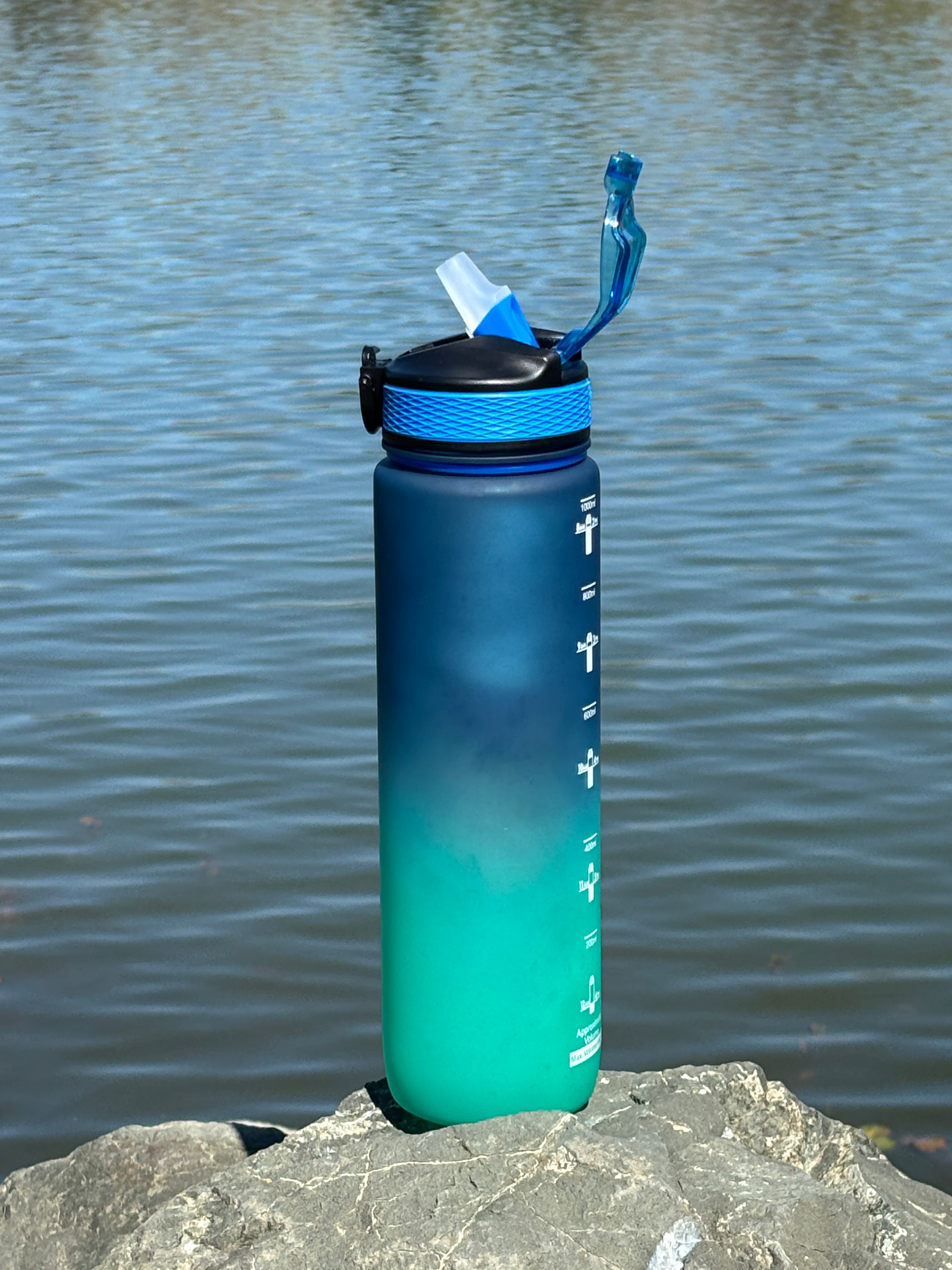 Blue and green water filter bottle on a stone surface with water in the background