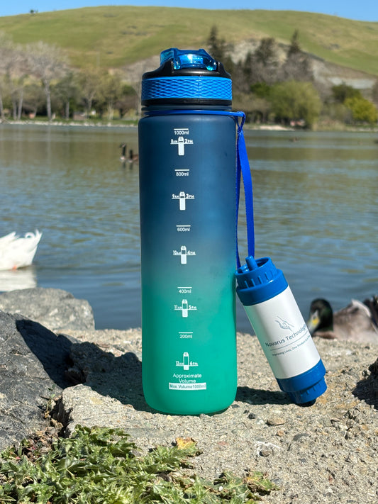 Gradient blue to green water bottle with blue cap on a concrete surface near a body of water.