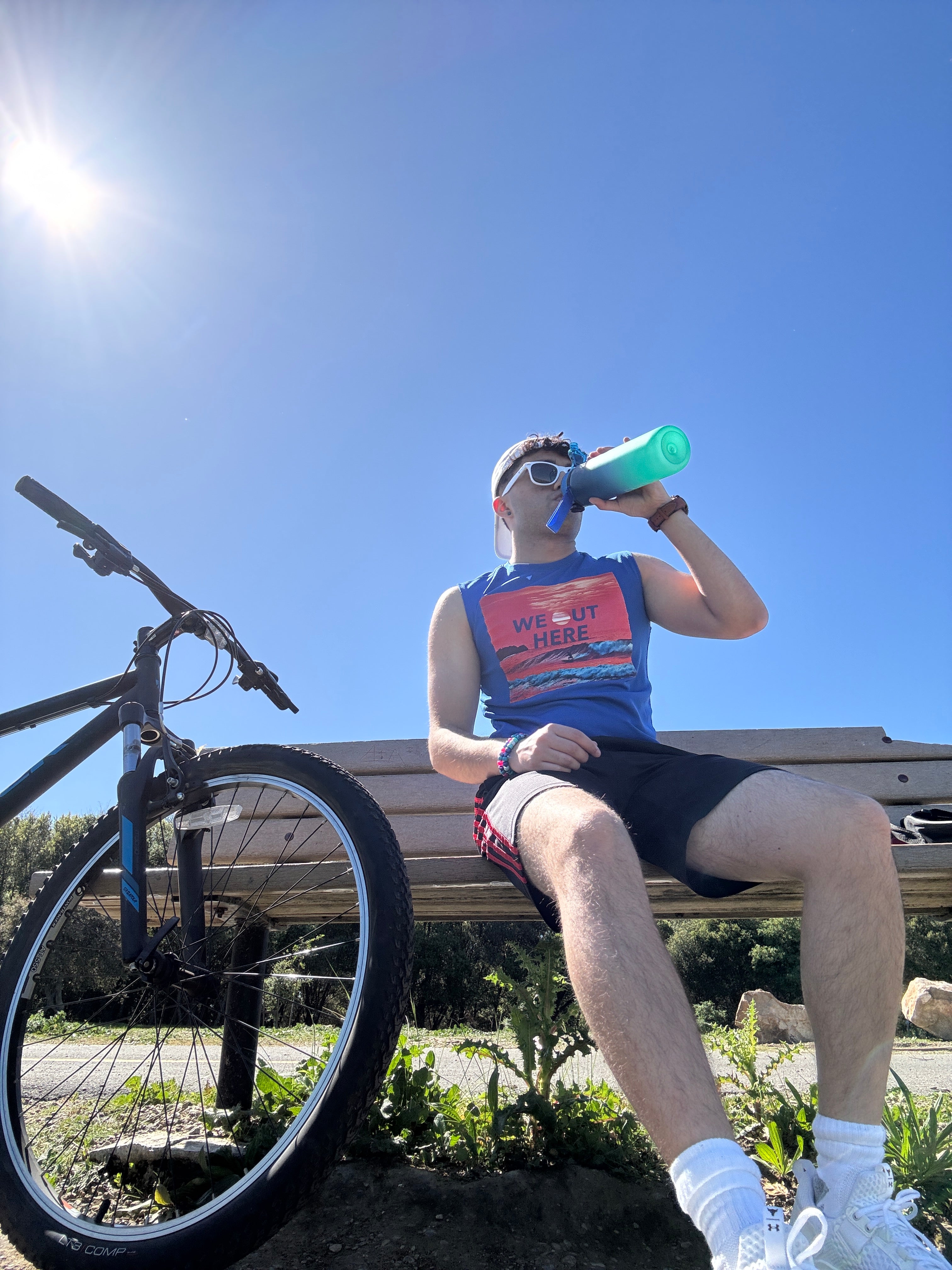 Person with a bicycle, holding a water bottle against a clear blue sky.